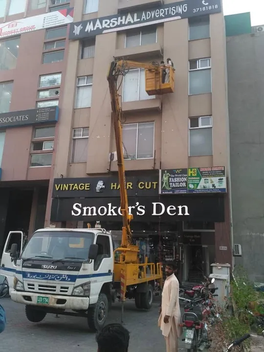 Crane truck lifting a Smoker's Den sign into place